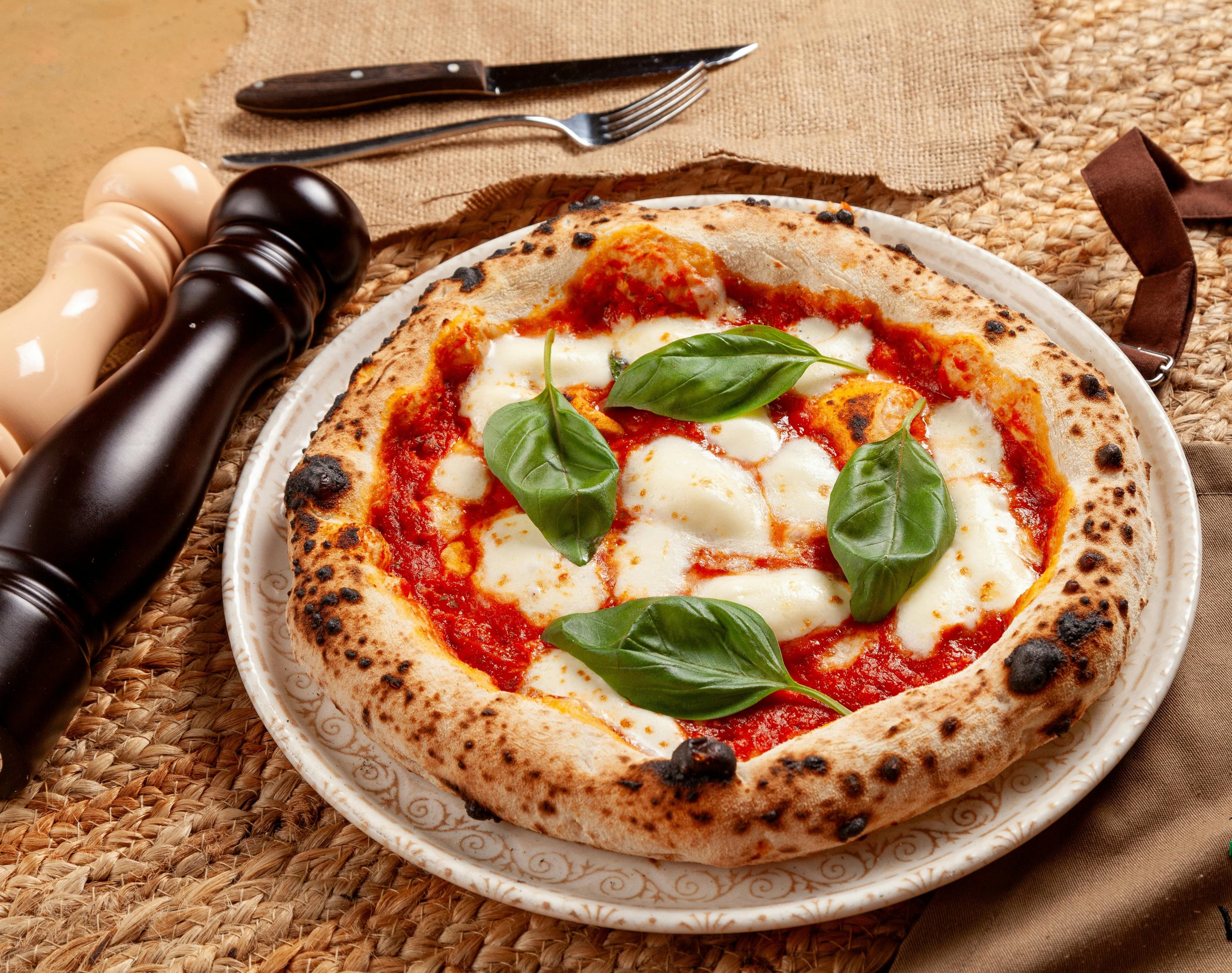 Wood-fired margherita pizza with a charred crust and fresh basil